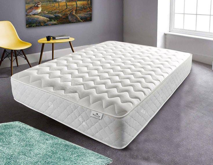 A white cooling mattress pad with a wave-patterned surface placed on a bed in a modern bedroom. The mattress is designed for comfort and temperature regulation, enhancing sleep quality.