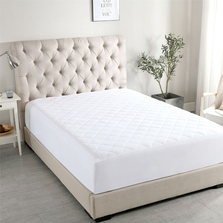 A neatly fitted white mattress pad on a stylish bed with a tufted beige headboard, showcasing one of the best mattress pads for comfort and protection in a modern bedroom setting.